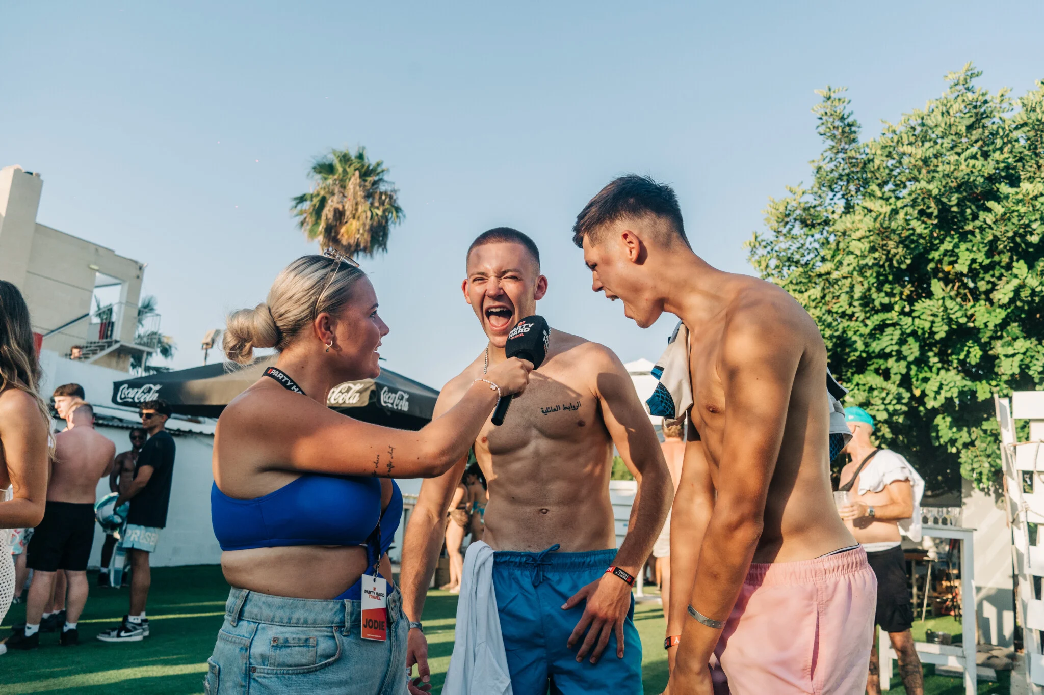 Party Hard Travel rep interviewing two excited lads at a Sunset sessions poolside event in Ayia Napa.