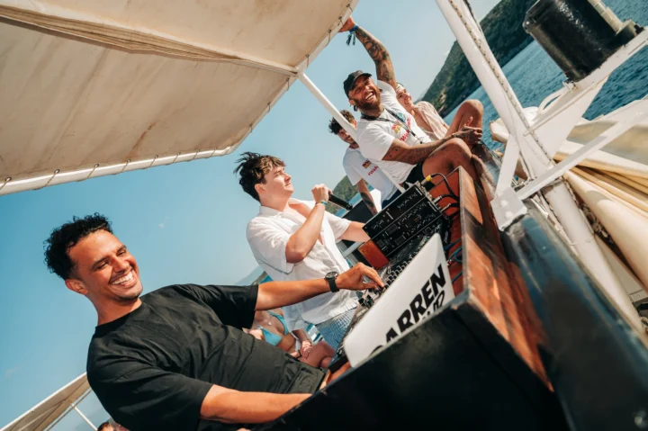 DJ Darren D on the decks bringing the energy on the Malia Booze Cruise as reps hype the crowd for a day of tunes and sea views.