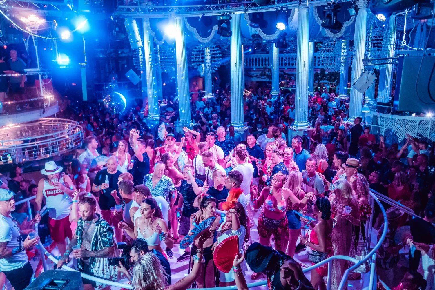 Crowd dancing at Es Paradis Ibiza under blue lights, packed floor, upbeat music and iconic summer club vibes.