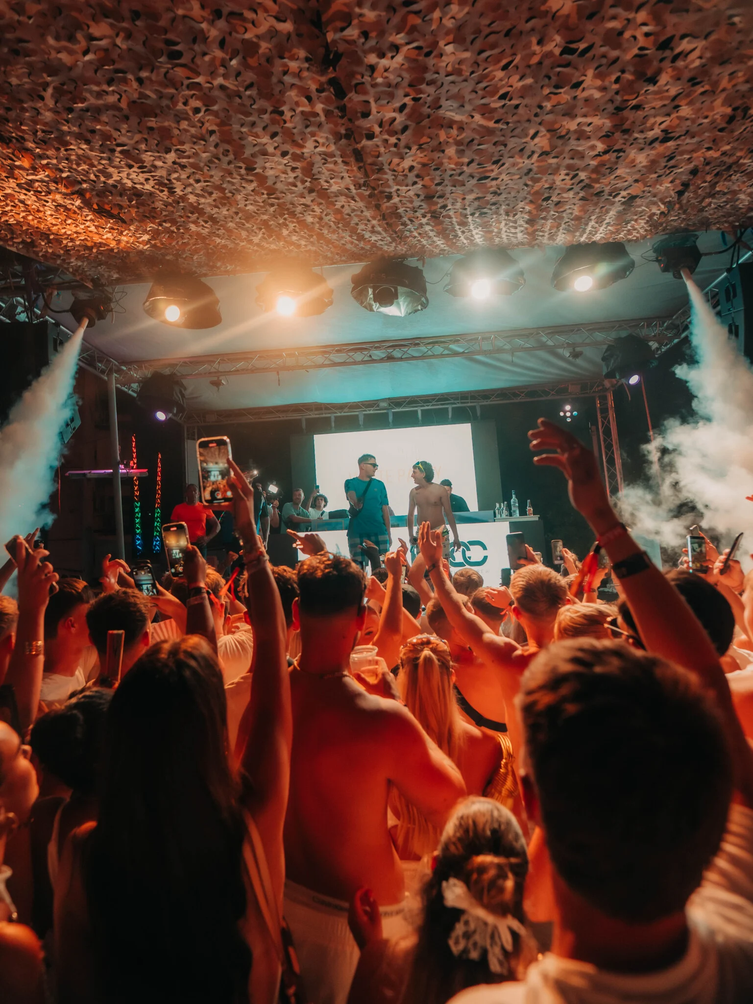 Crowd at Ayia Napa Agenda White Party dancing with DJs on stage, smoke effects and vibrant lights filling the venue atmosphere