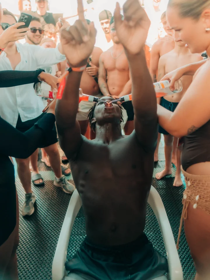 Partygoer at an Ayia Napa boat party taking part in drinking games with friends cheering and capturing the moment