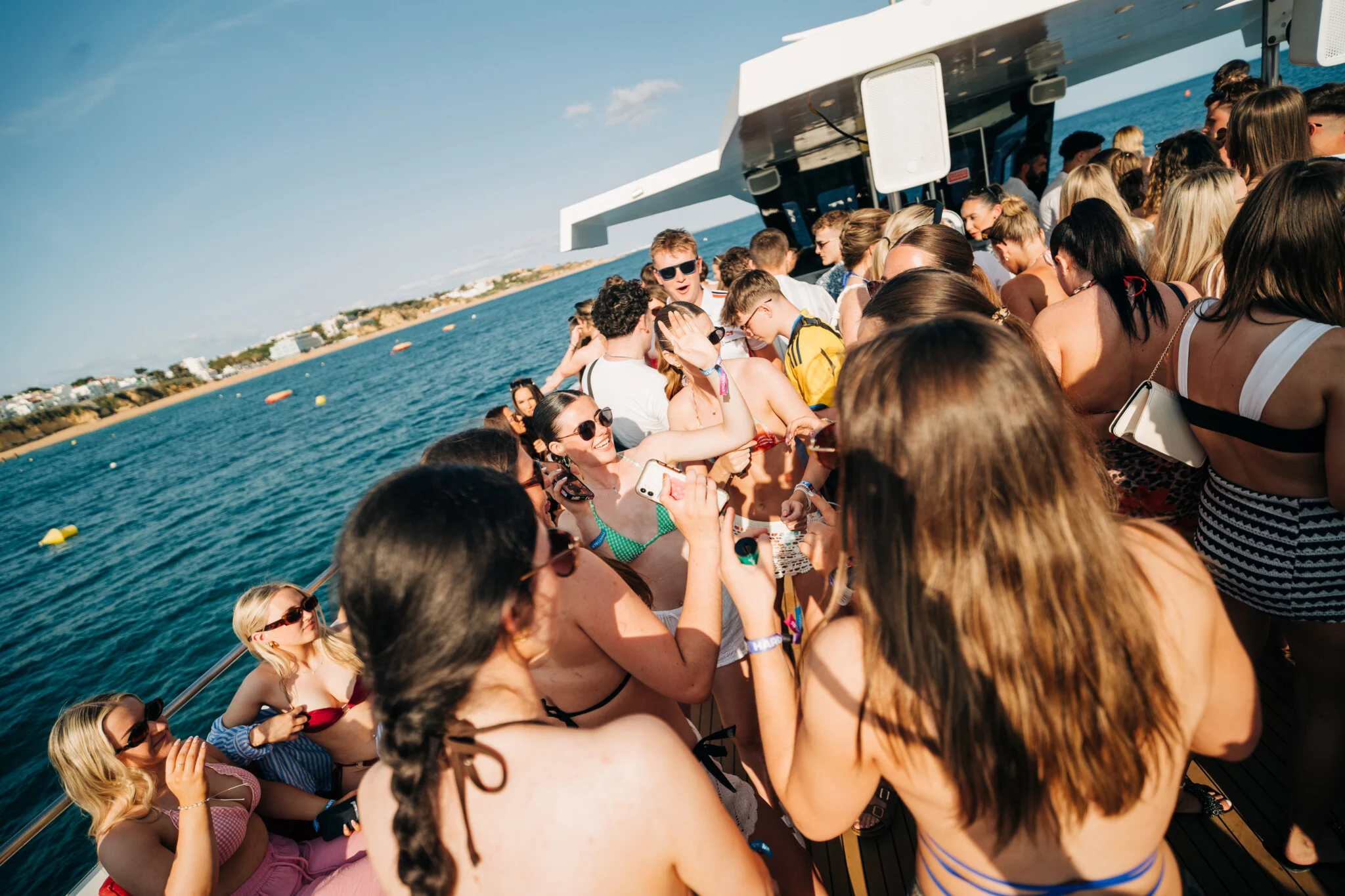 Girls and lads enjoying the Albufeira Boat Party in Albufeira, dancing on deck with drinks, music and stunning ocean views in the background.