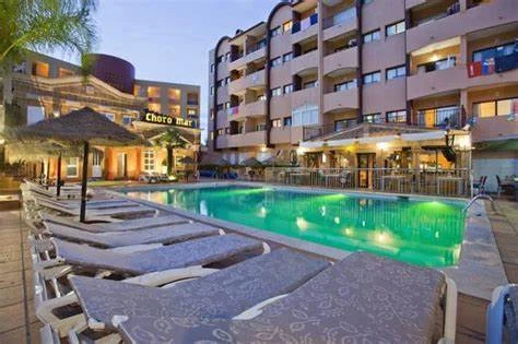 Evening view of Choromar Apartments in Albufeira featuring a lit outdoor swimming pool, sun loungers, and surrounding balconies.