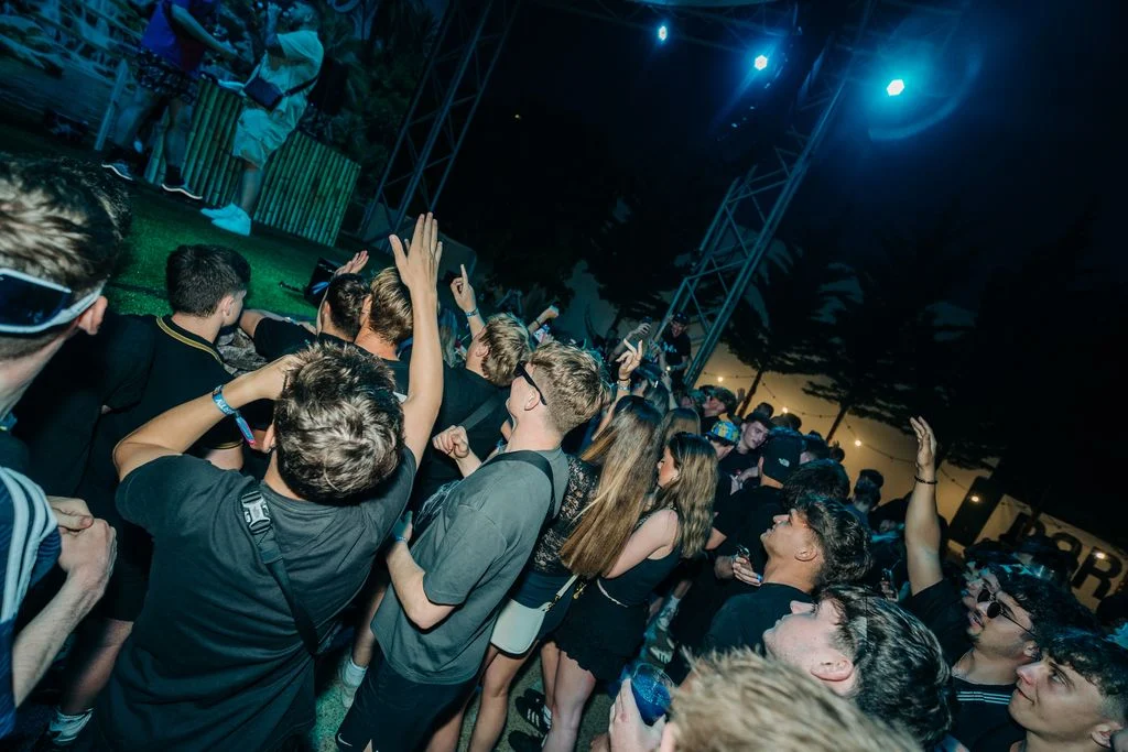 Crowd partying under blue lights at Agenda Beach Club in Albufeira, hands in the air as the DJ keeps the energy high.