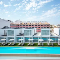 Oura Senses Apartments in Albufeira with a modern white exterior, private terraces, sun loungers, parasols, and a long outdoor swimming pool.