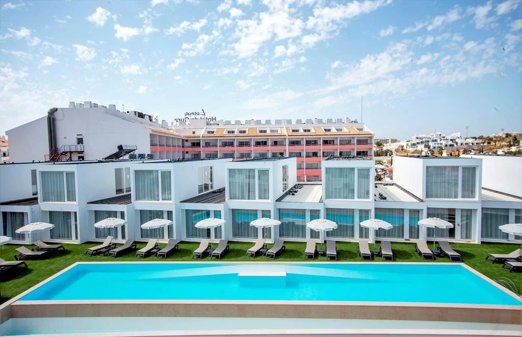 Oura Senses Apartments in Albufeira with a modern white exterior, private terraces, sun loungers, parasols, and a long outdoor swimming pool.
