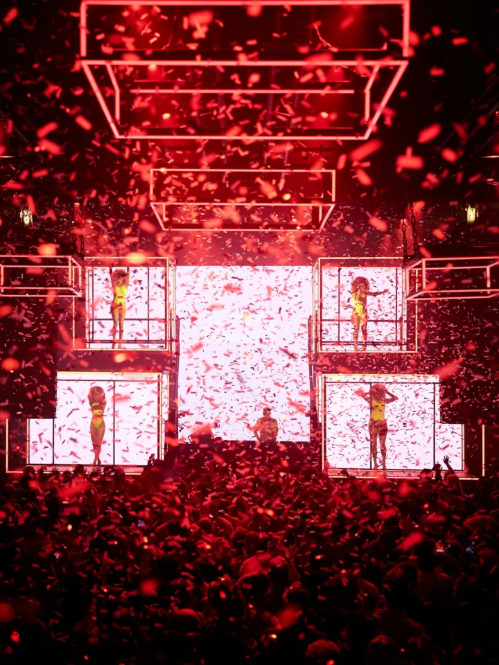 Epic Ibiza nightclub scene with confetti, dancers, and a packed crowd under red lights at Glitterbox.