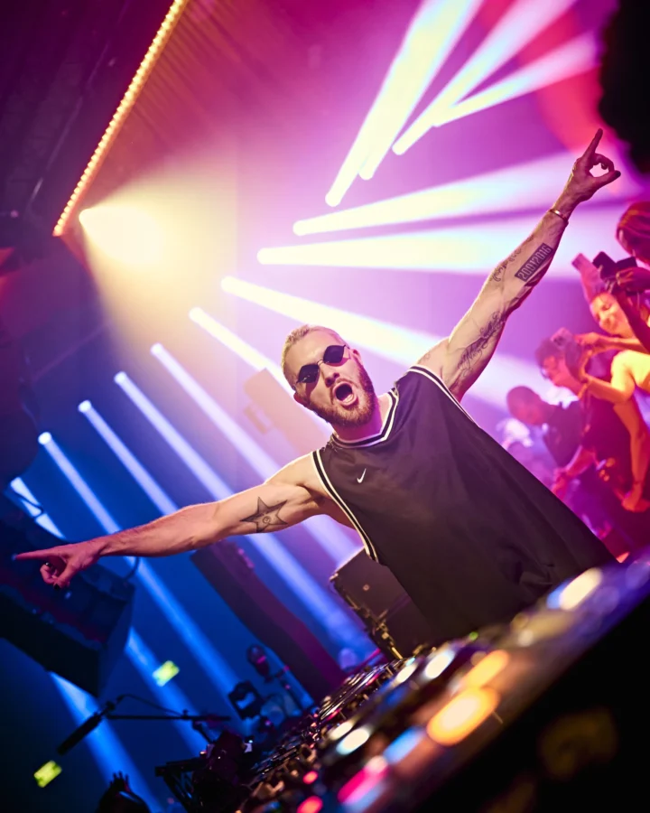 DJ hyping the crowd at a packed Ibiza club with bright lights, huge energy and non-stop party vibes.