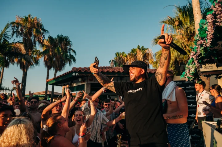 Crowd going off at a Malia pool party as the host hypes the crowd under the sun, with drinks, music and pure summer vibes.