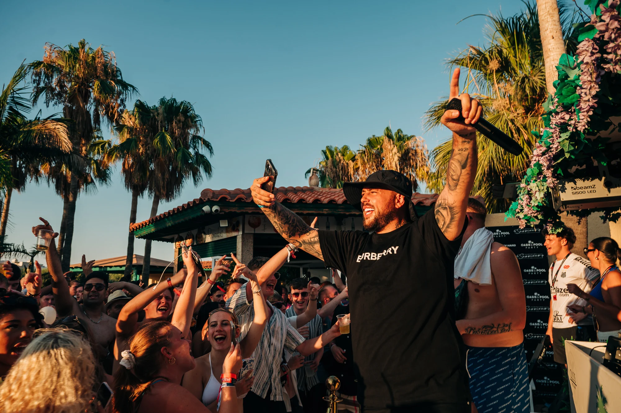Crowd going off at a Malia pool party as the host hypes the crowd under the sun, with drinks, music and pure summer vibes.