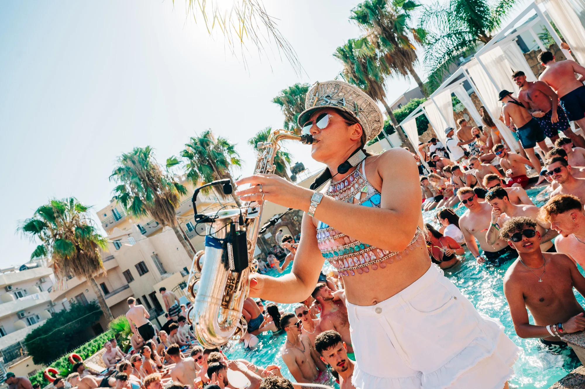 Pool party vibes in Malia as the sax player brings the beats to a crowd of partygoers dancing under the summer sun.
