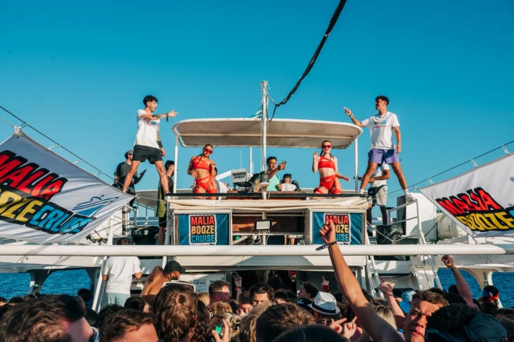 Crowds partying under the sun on the Malia Booze Cruise with DJs, dancers, drinks and unreal summer energy at sea.