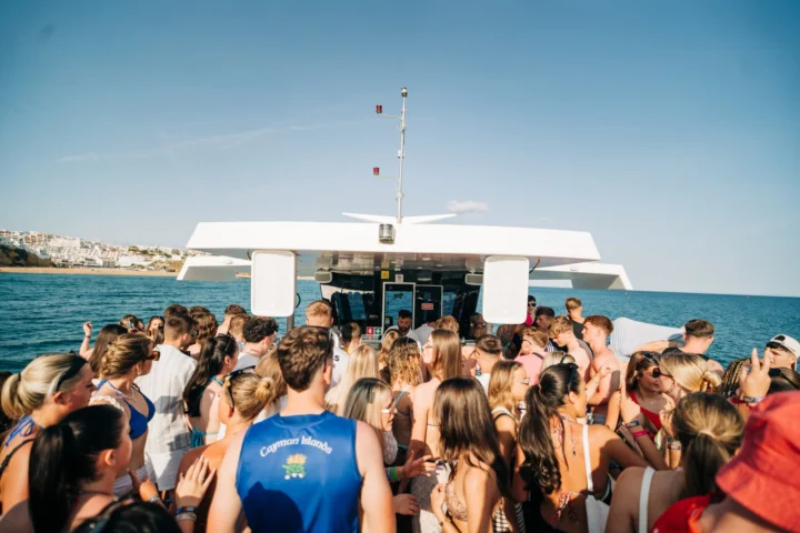 Crowd of lads and girls dancing on deck with a DJ at the Albufeira Boat Party, enjoying music, sunshine, and views of the Algarve coastline.