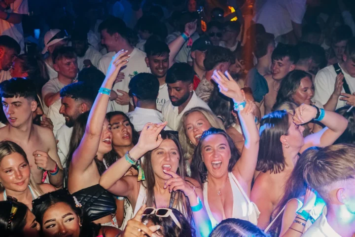 Lads and girls packed into a Barcelona club, arms up and shouting as the room erupts with full-on party energy.