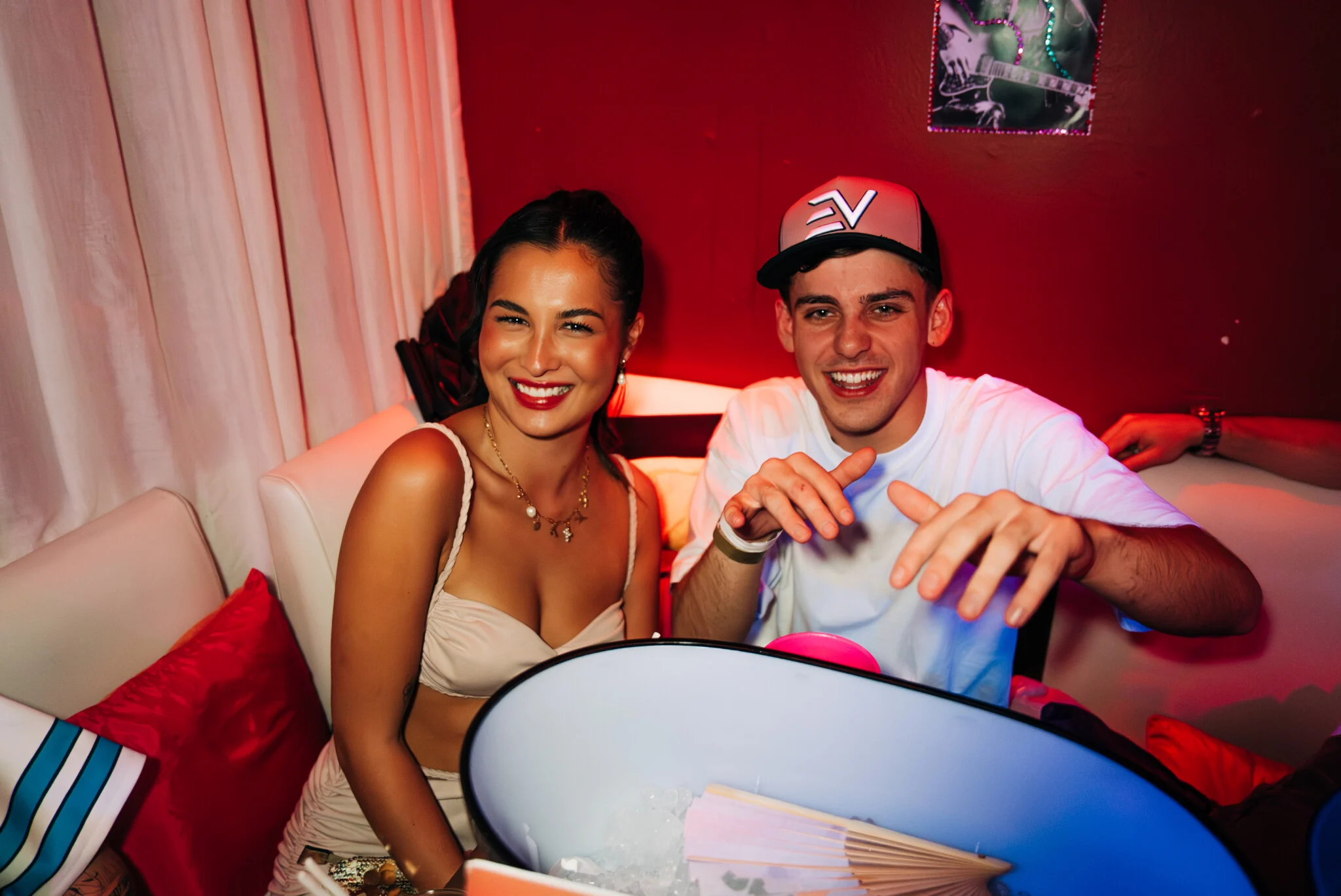 Smiling pair at Carpe Diem Barcelona chilling in VIP seating with neon light glow kicking off a lively night.