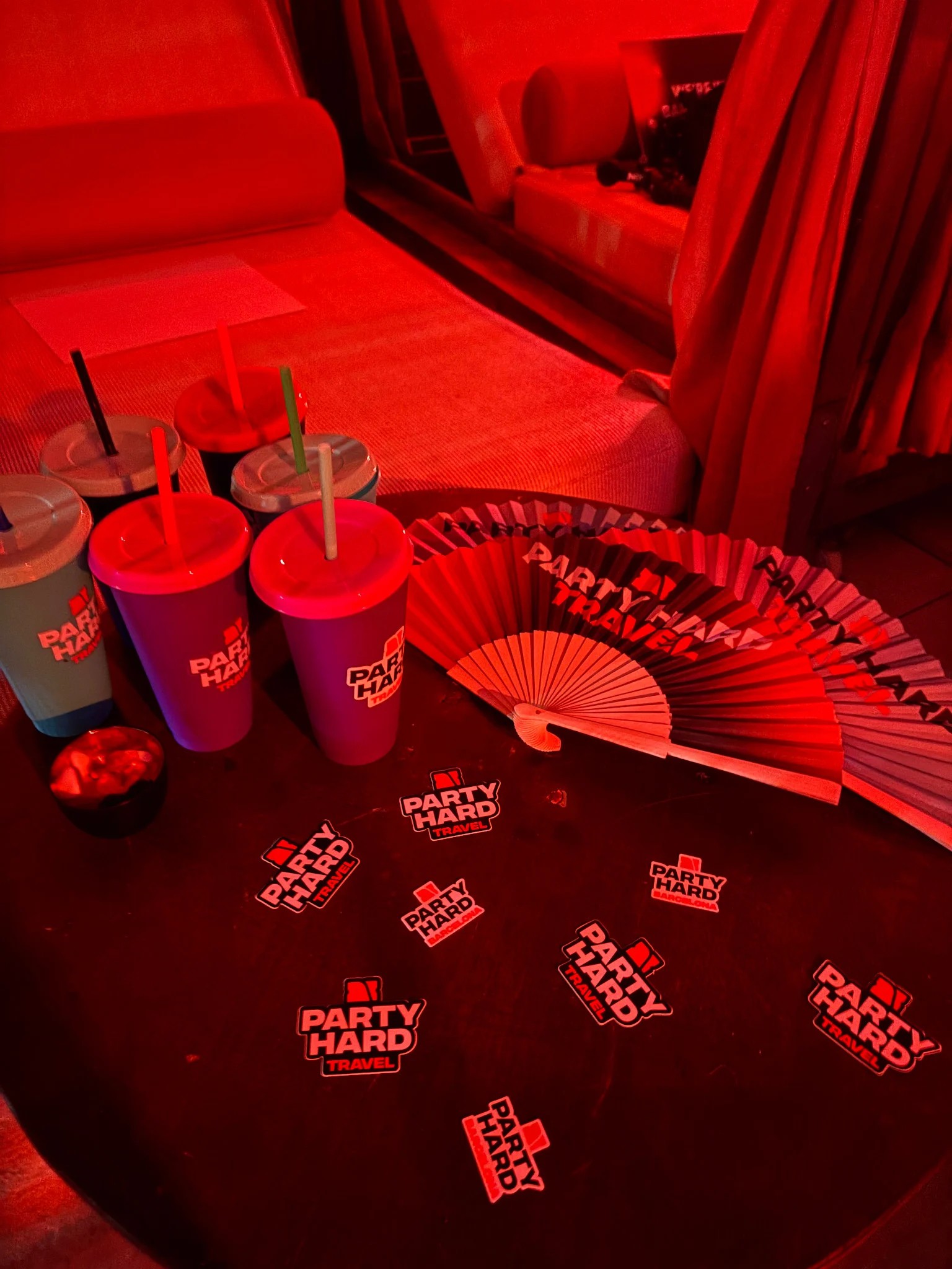 Party Hard cups, fans and stickers laid out on a red-lit club table in Barcelona, setting up the vibe before the night kicks off.