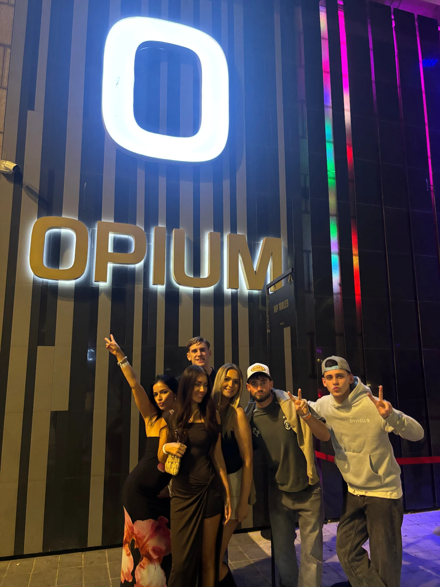 Outside Opium Barcelona, a group of lads and girls pose under the bright club signage, ready for a big night ahead.
