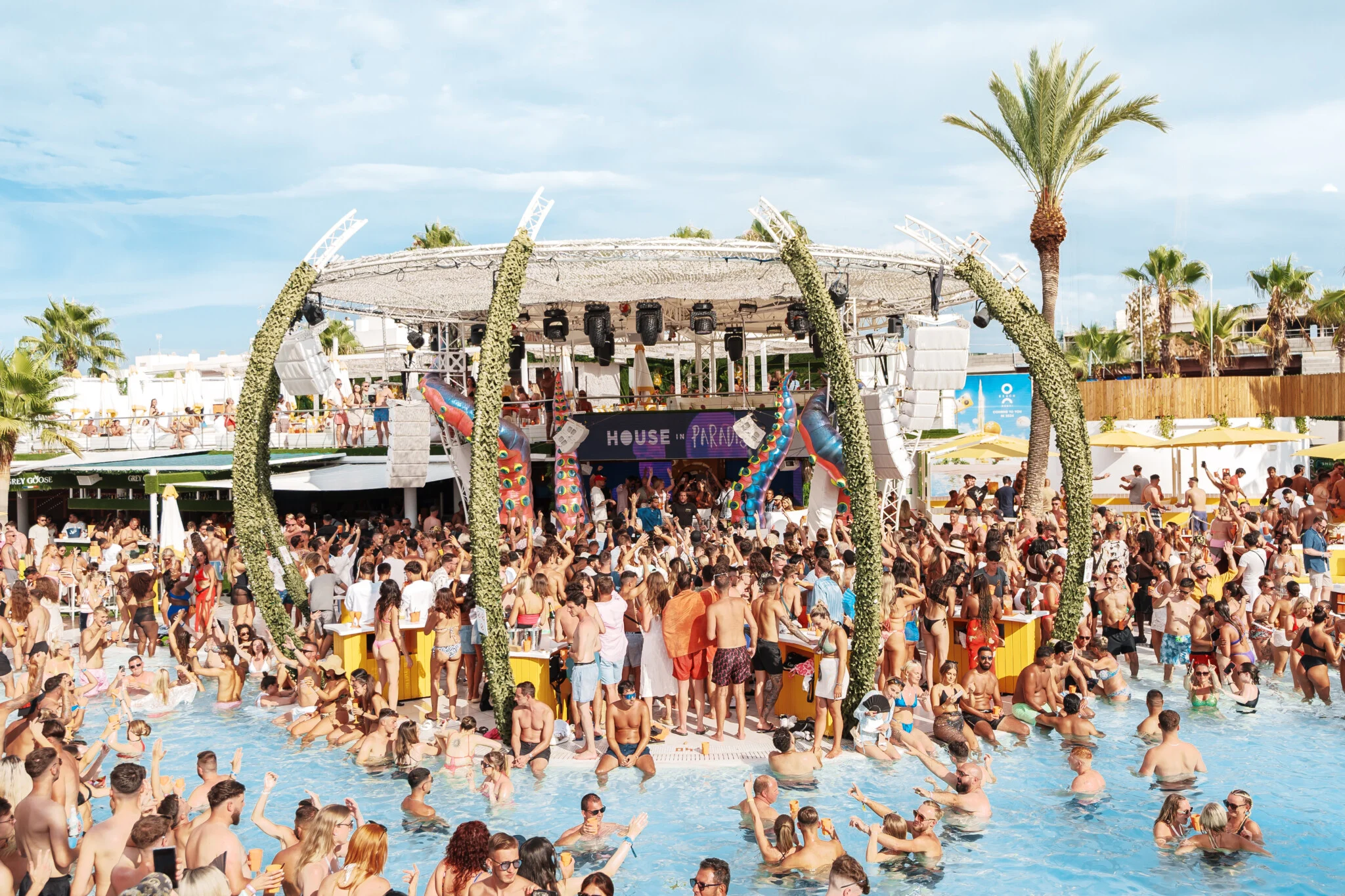 Wide view of House in Paradise at O Beach Ibiza with a packed pool, crowded stage area and people dancing across the venue